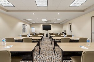 A conference room with multiple tables, chairs, a large screen, and a patterned carpet.