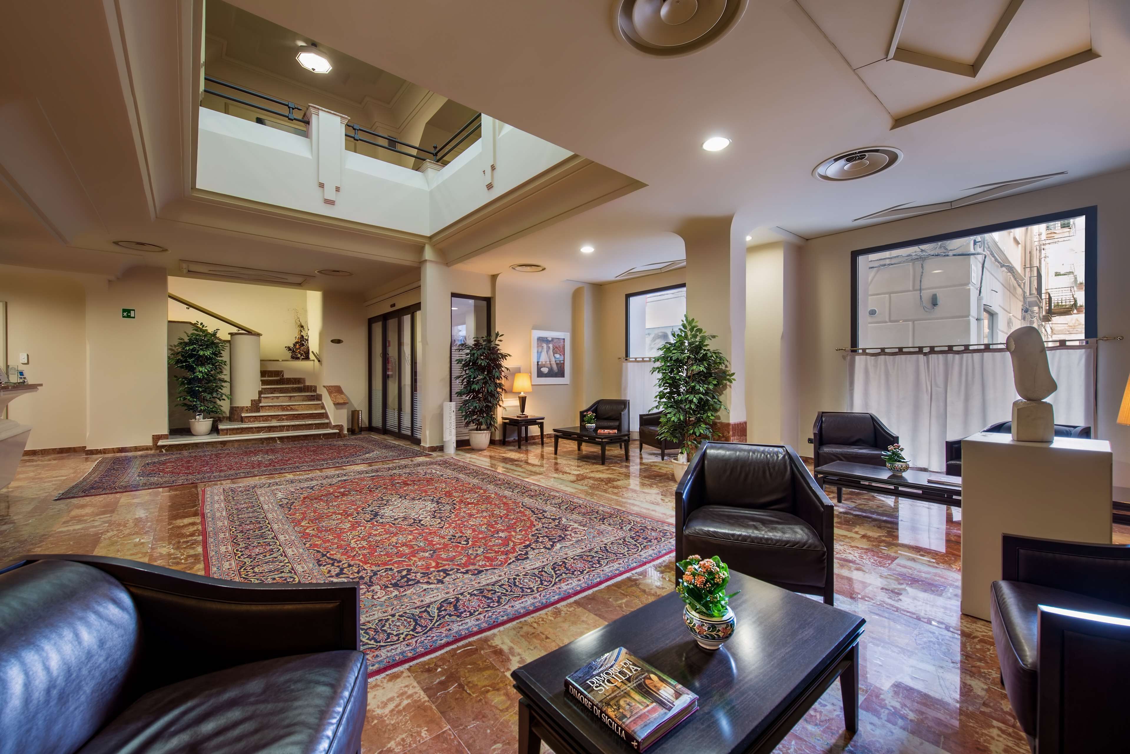 A spacious lobby with a large carpet, leather seating, a staircase, and a large window.