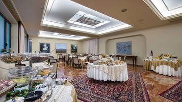 Uma ampla sala de banquetes com pé direito alto, claraboias e uma mesa redonda central com toalha branca.