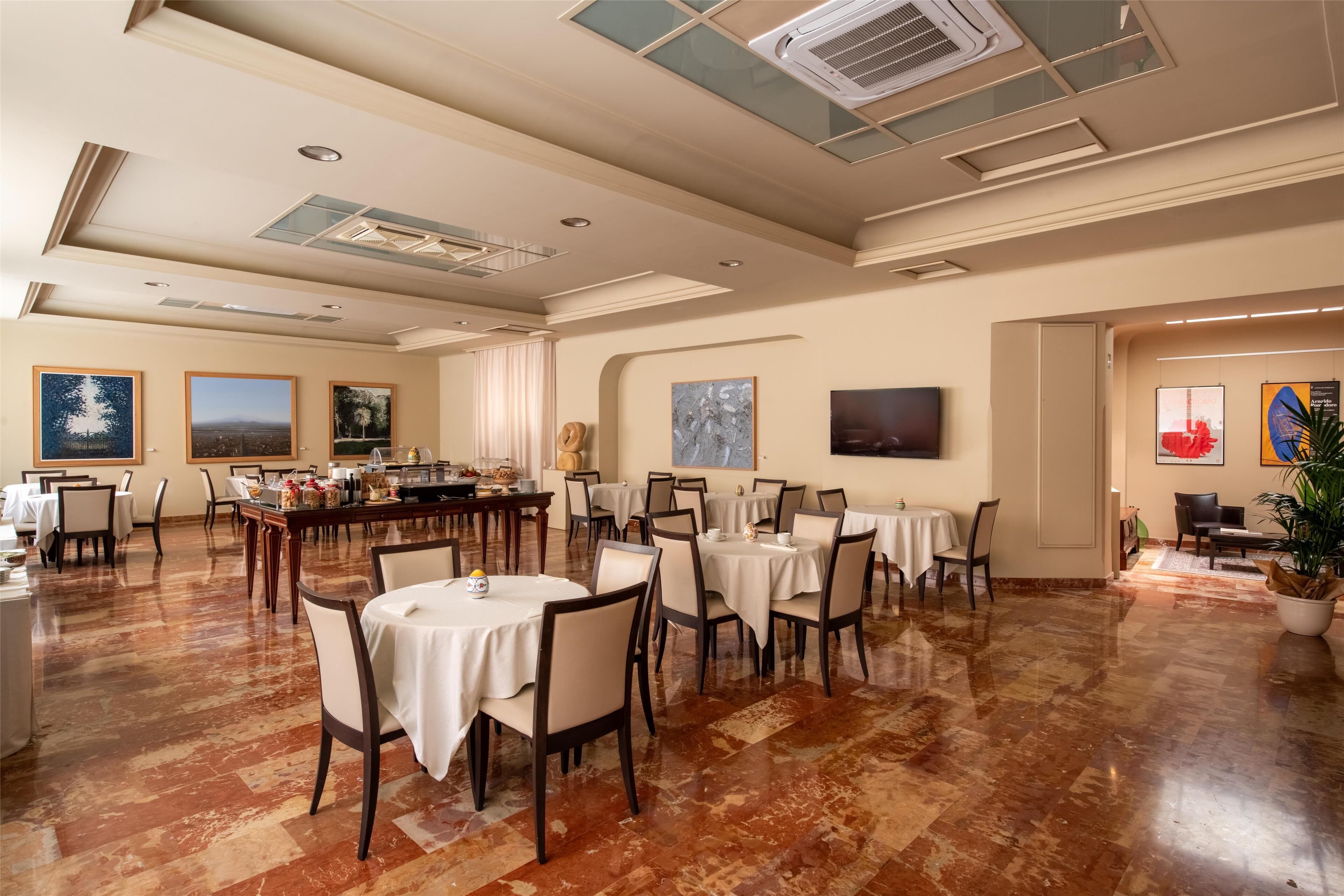 A spacious dining area with multiple tables and chairs, a ceiling with skylights, and artwork on the walls.