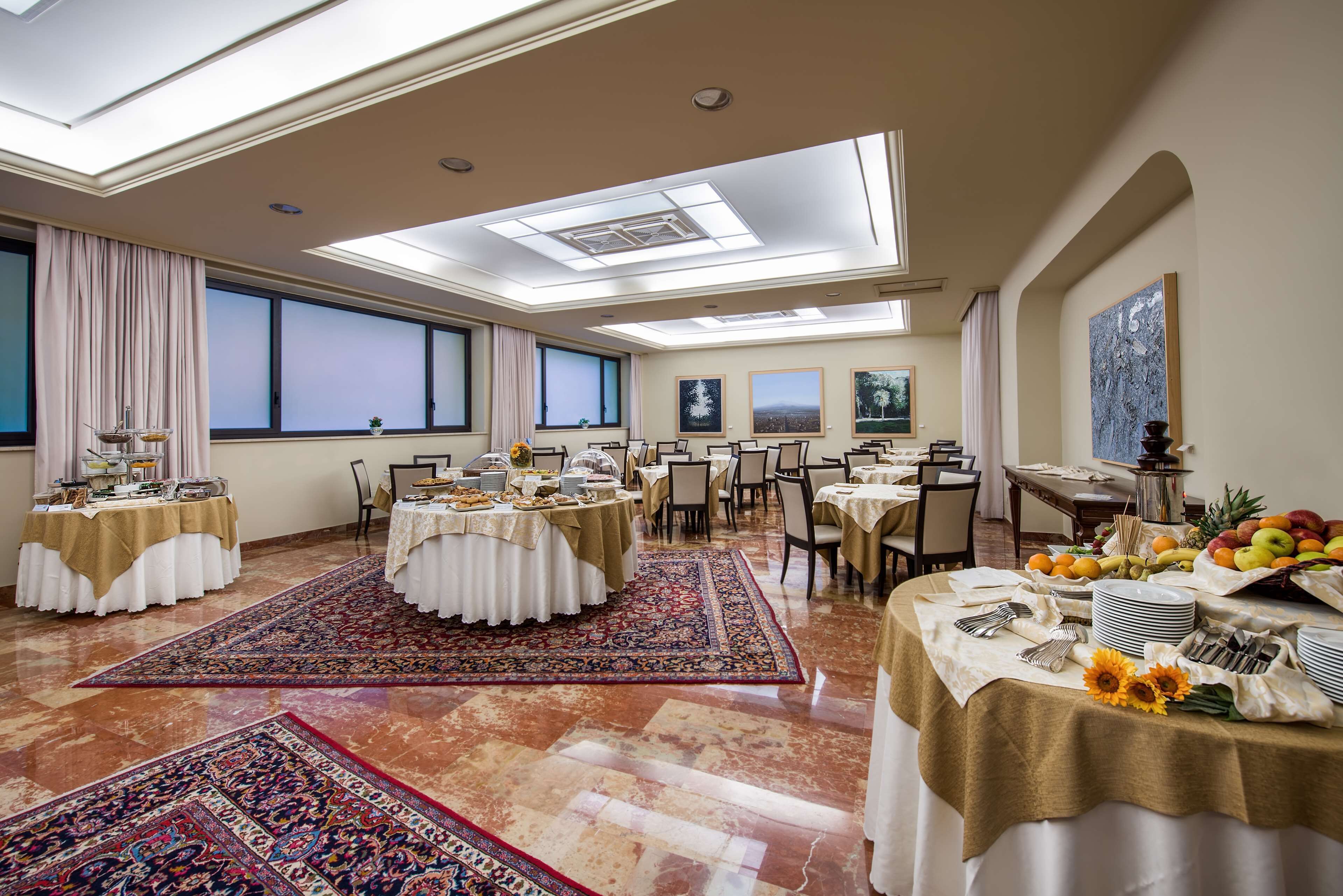 A spacious dining area with round tables, a large rug, and a view of the city through large windows.