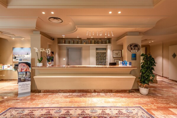 A hotel reception area with a marble floor, a reception desk, a large potted plant, and a decorative wall clock. - Best Western Hotel Stella D'Italia (Marsala)