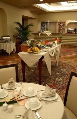 A dining area with round tables set for a meal, a buffet table with fruits and beverages, and a potted plant. - Best Western Hotel Stella D'Italia (Marsala)