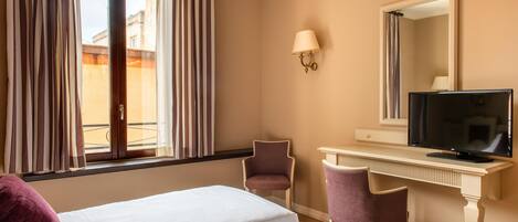 A hotel room with two beds, a desk with a television, a chair, and a window with curtains.