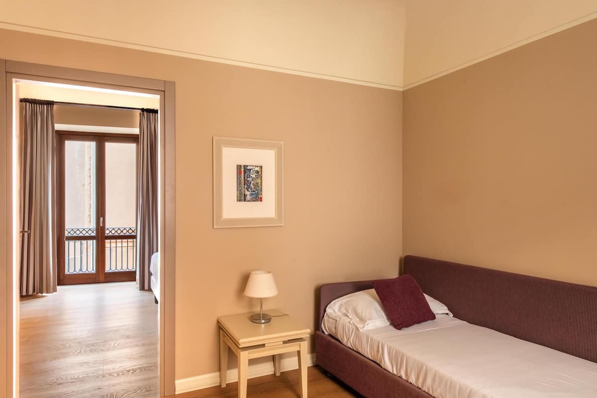 A hotel room with a bed, a bedside table with a lamp, a framed picture on the wall, and a view of the balcony.