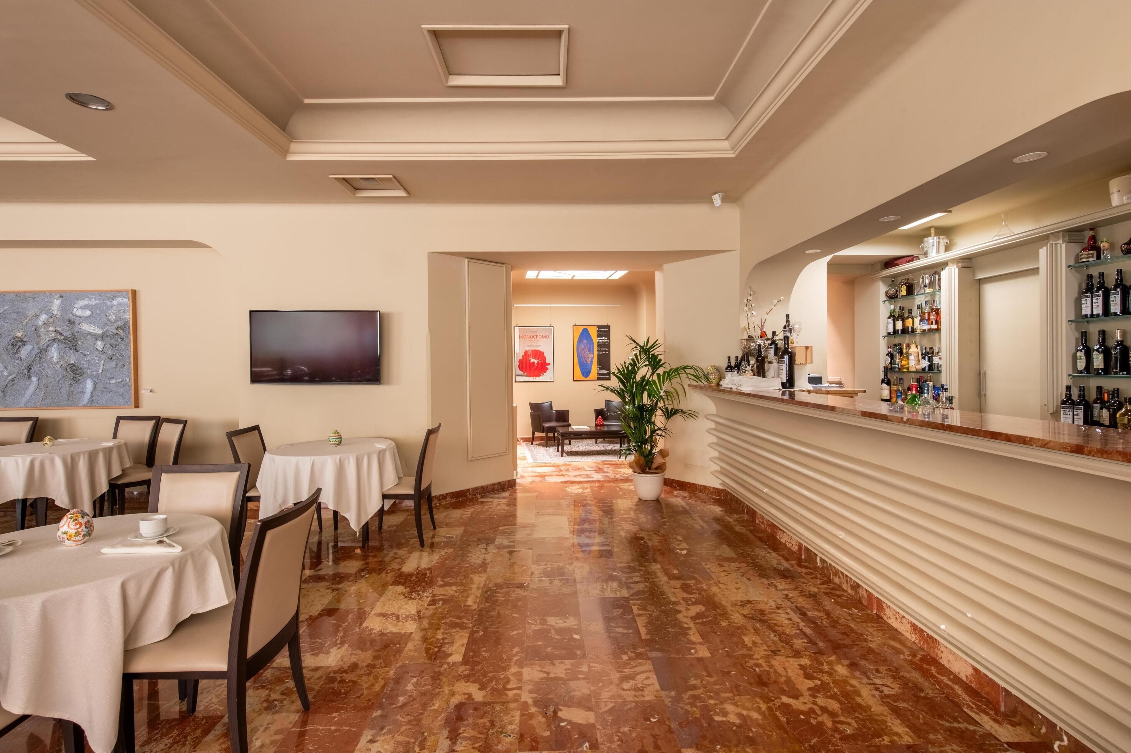 Un hall de hotel con mesas, sillas, una zona de bar y un televisor.