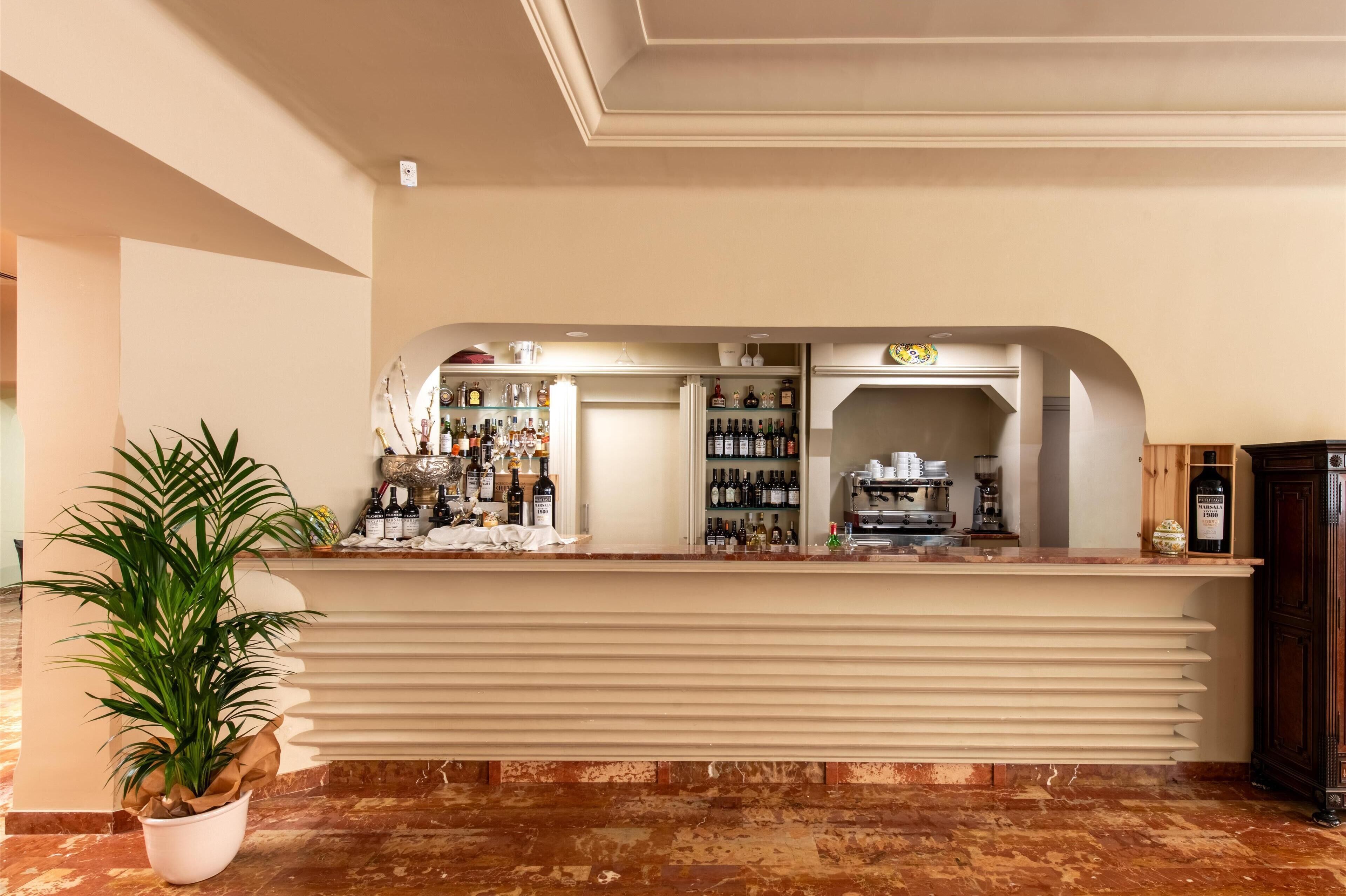 Una zona de bar con suelo de mármol, una planta en maceta y estanterías llenas de botellas.