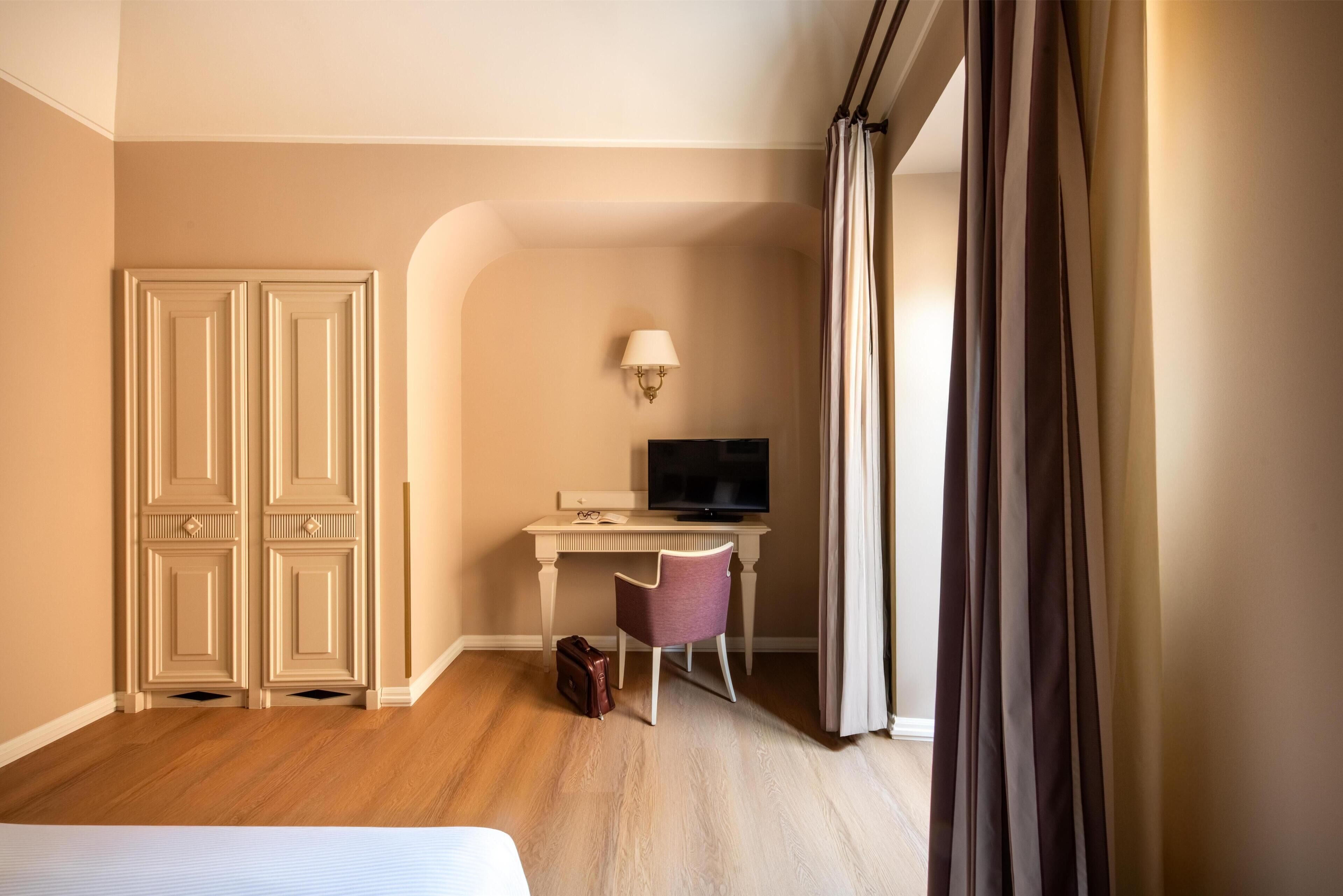 Una habitación de hotel con cama, escritorio, silla, televisor y armario.