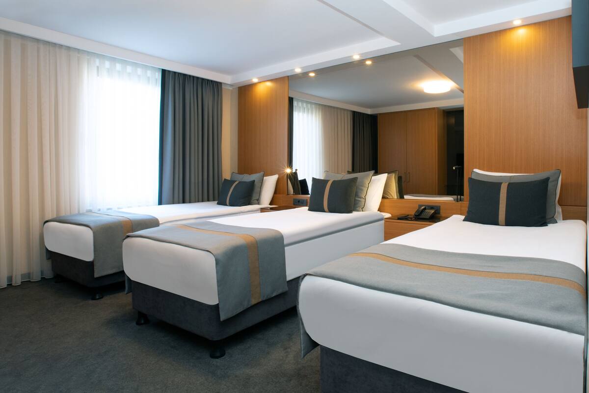 A hotel room with two single beds, a double bed, and a small sofa.