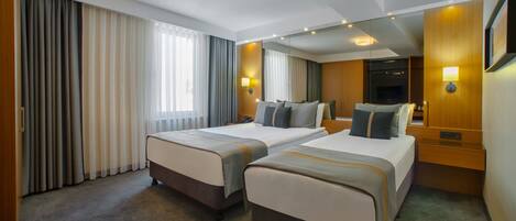 Habitación de hotel con dos camas, un ventanal con cortinas, un televisor de pantalla plana y una pared de acento de madera.