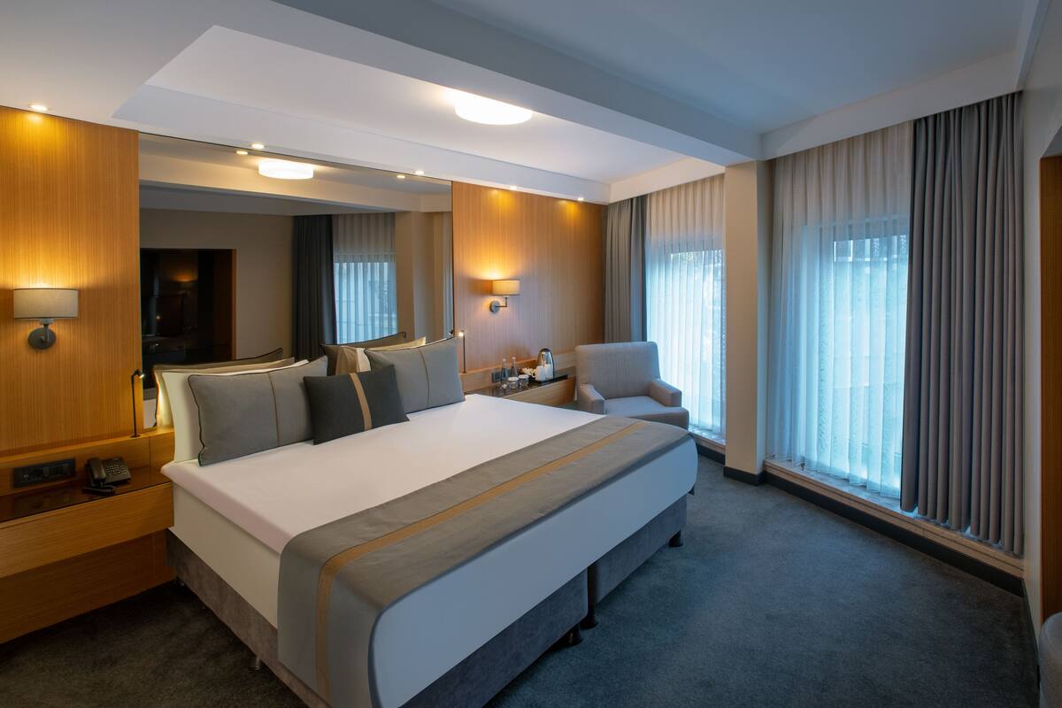 A hotel room with a large bed, a desk with a phone, a chair, and a large window with curtains.