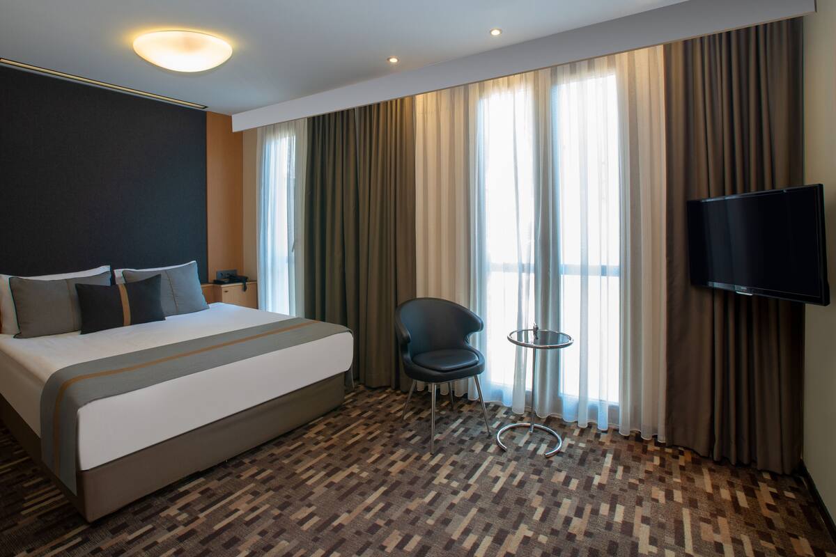 A hotel room with a large bed, a TV, a chair, and a small table.