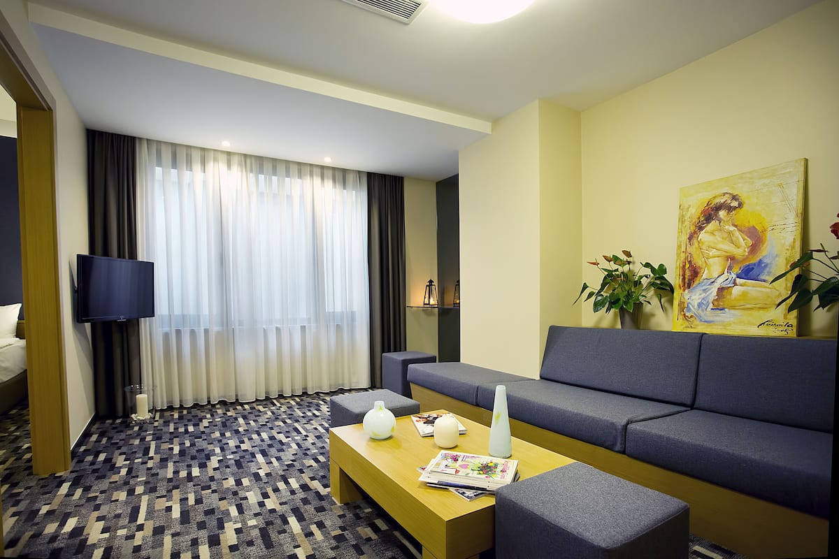 A hotel room with a sofa, a coffee table, a TV, and a painting on the wall.