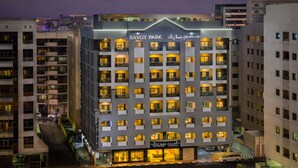 A multi-story hotel with balconies, a sign reading "SAVOY PARK," and a parking area in front.