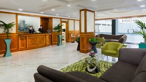 A hotel lobby with a reception desk, seating area, and large windows.