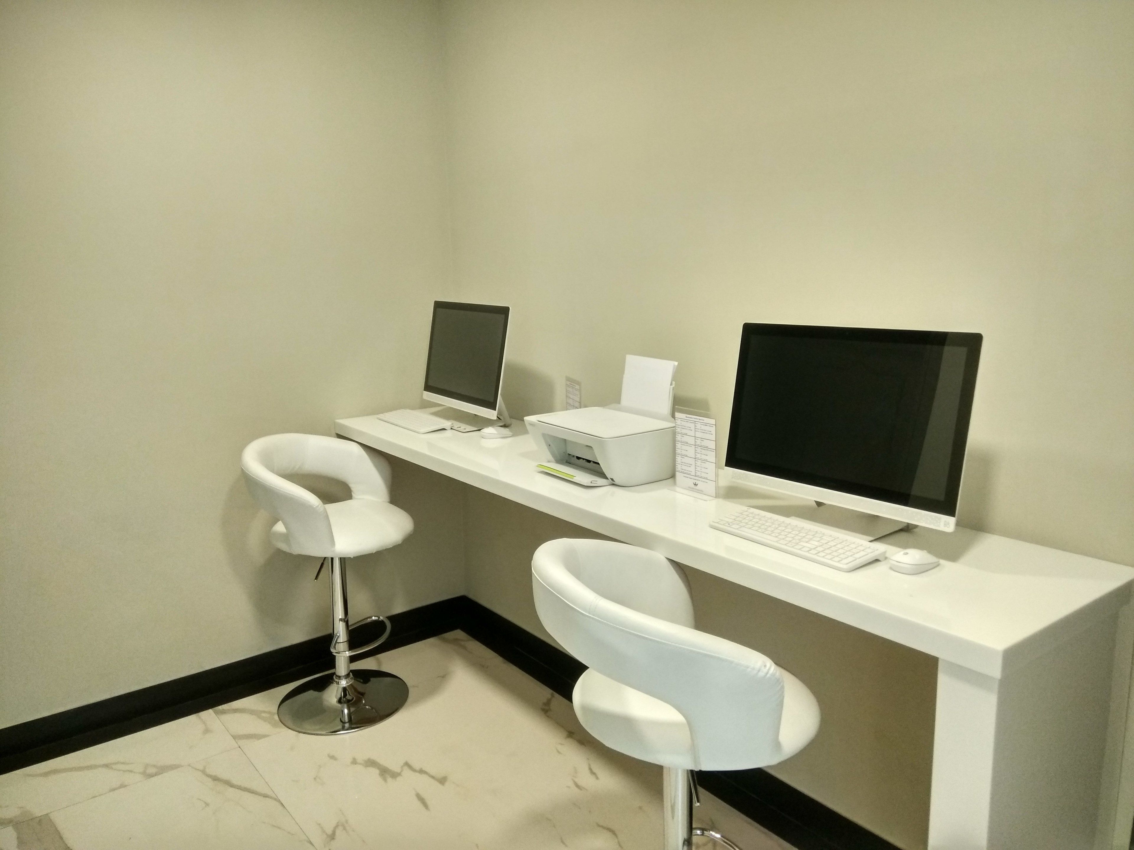 A modern office space with a white desk, two computer monitors, a keyboard, and two white chairs.