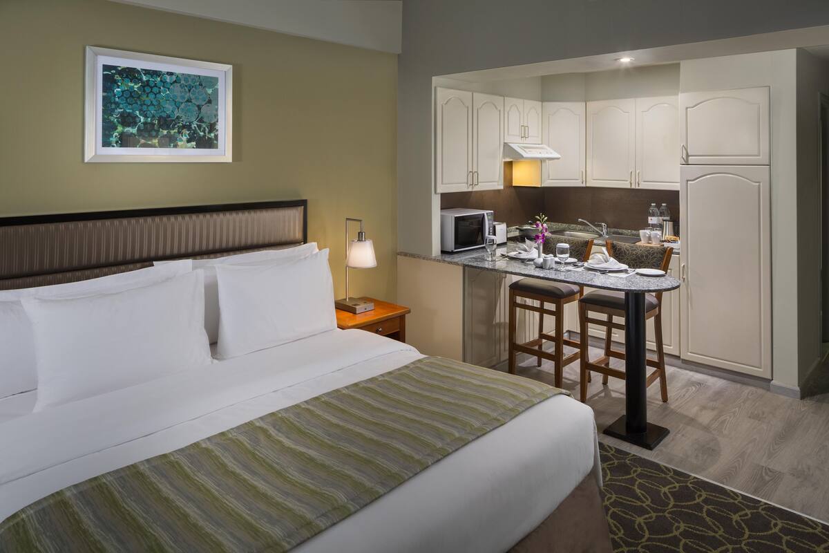 A hotel room with a bed, a small kitchenette, and a dining area.