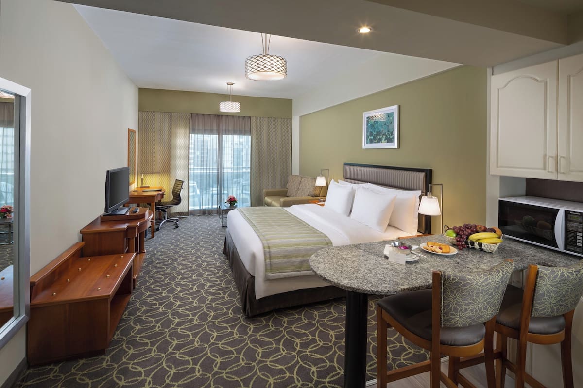 A hotel room with a bed, desk, chair, dining table, and a microwave.