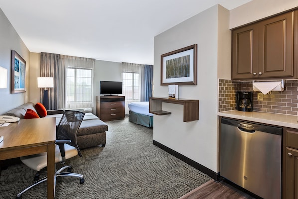 Habitación de hotel con comedor, kitchenette, televisor y cama.