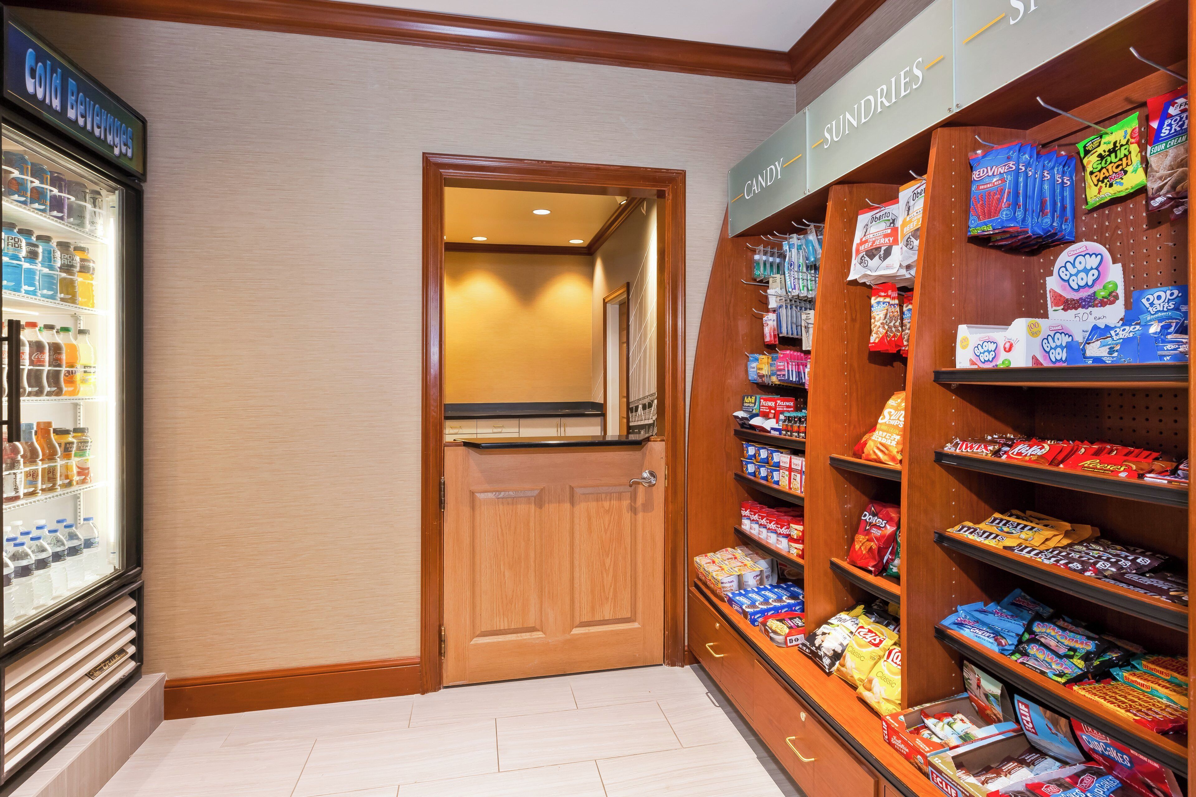 Un pasillo de hotel con un expositor de bebidas refrigeradas, una sección de dulces y una puerta que da a otra zona.