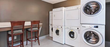 A laundry room with stacked washers and dryers, wooden chairs, and a light fixture on the ceiling.