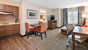 A hotel room with a kitchenette, a dining area with two chairs, a TV, and a window with curtains. - Staybridge Suites Kalamazoo by IHG (Kalamazoo)