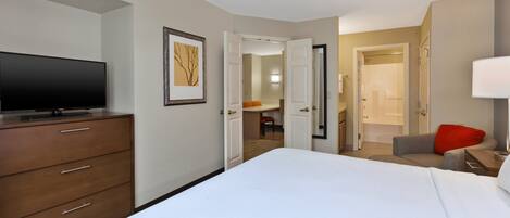 Habitación de hotel con una cama grande, un televisor sobre un tocador de madera, un cuadro enmarcado en la pared y una puerta que da al baño.