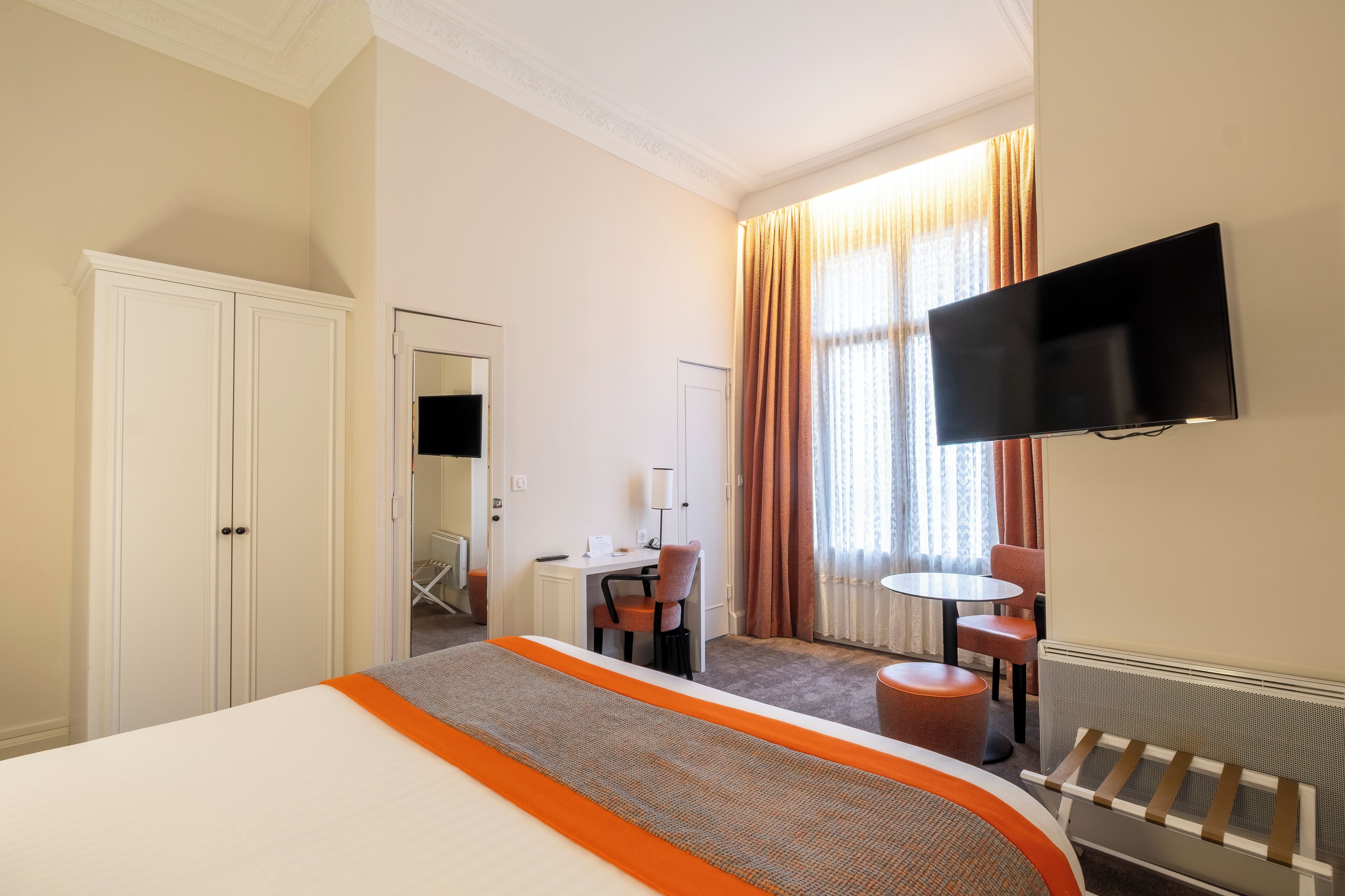 A hotel room with a bed, a desk, a chair, a TV, and a window with curtains.