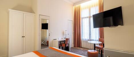 Habitación de hotel con cama, escritorio, silla, televisor y ventana con cortinas.