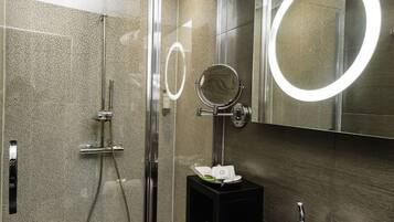 Une salle de bain moderne avec une douche à parois de verre, un lavabo noir avec un miroir et un miroir rond avec un éclairage intégré.