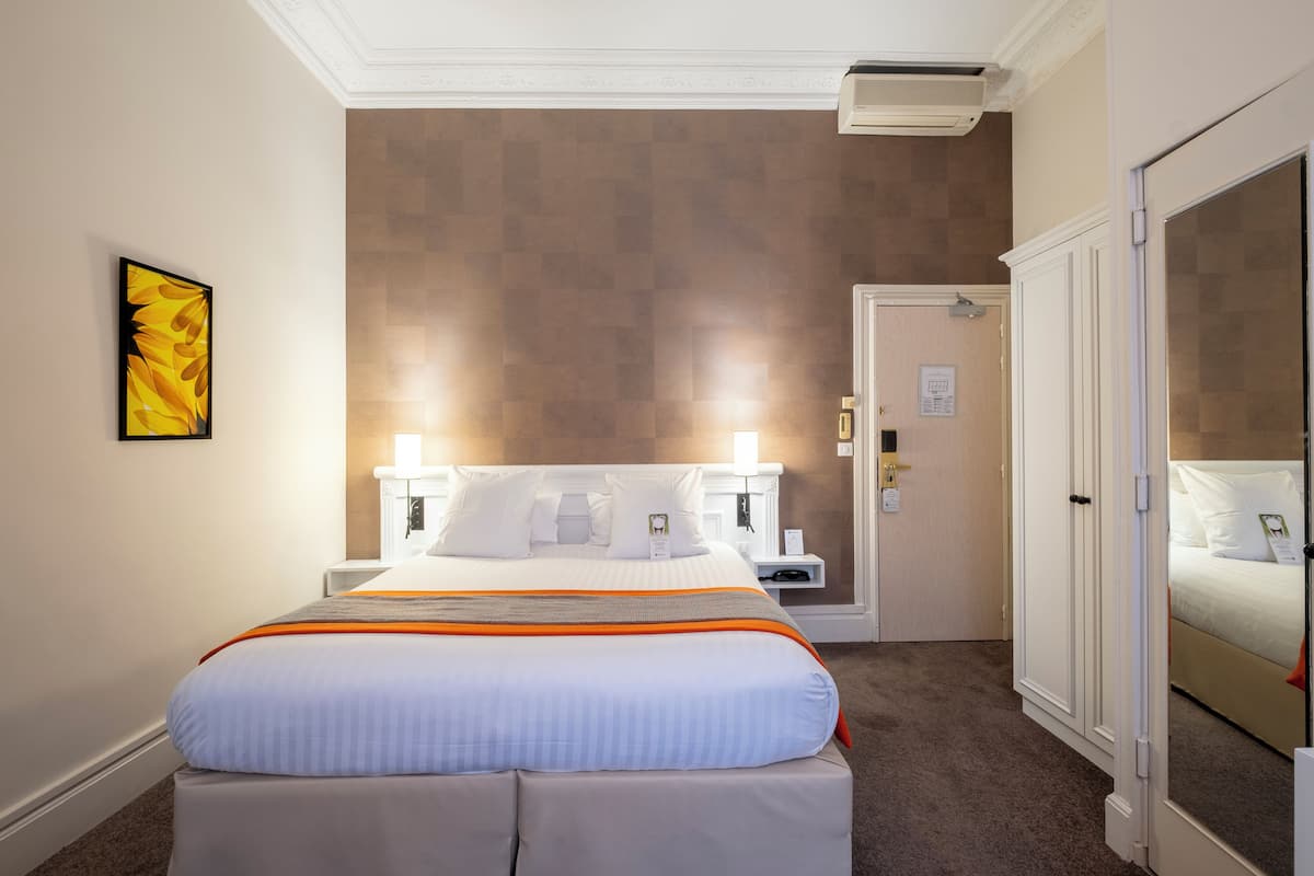 A hotel room with a large bed, a nightstand, a wardrobe, and a wall-mounted air conditioner.