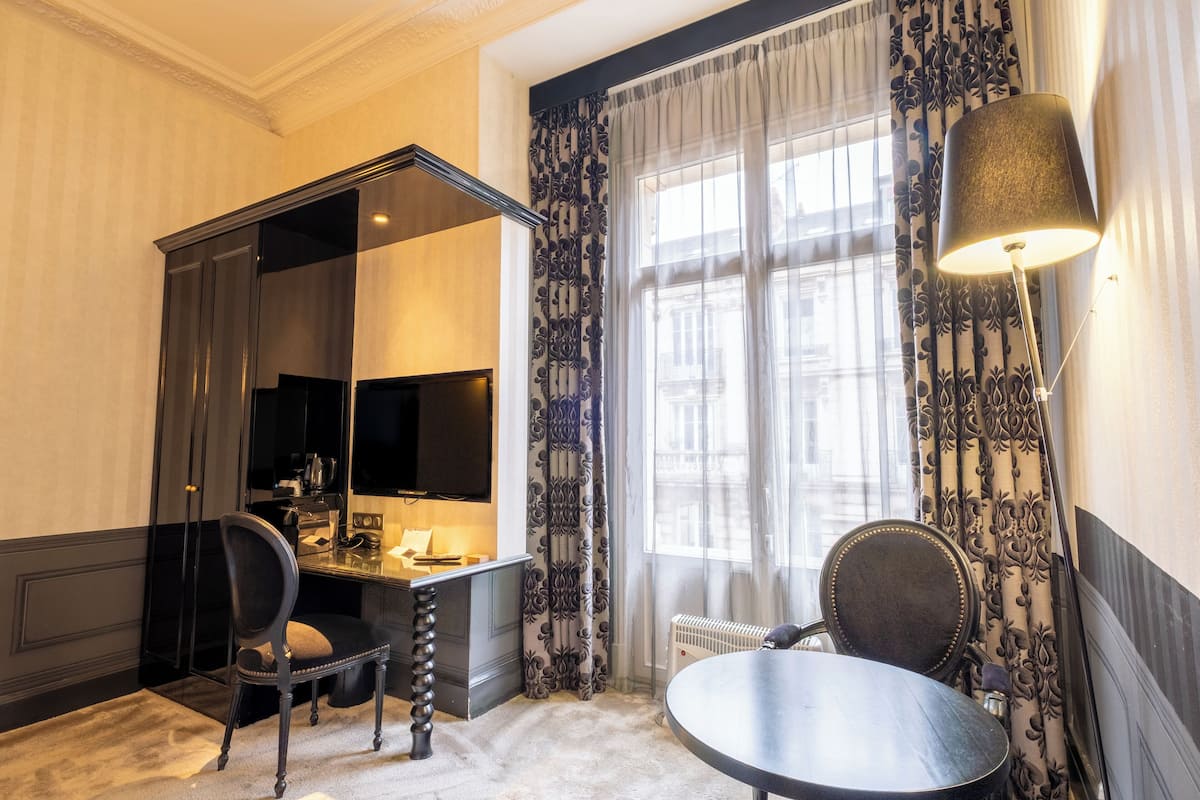 A hotel room with a desk, chair, and a large window with curtains.