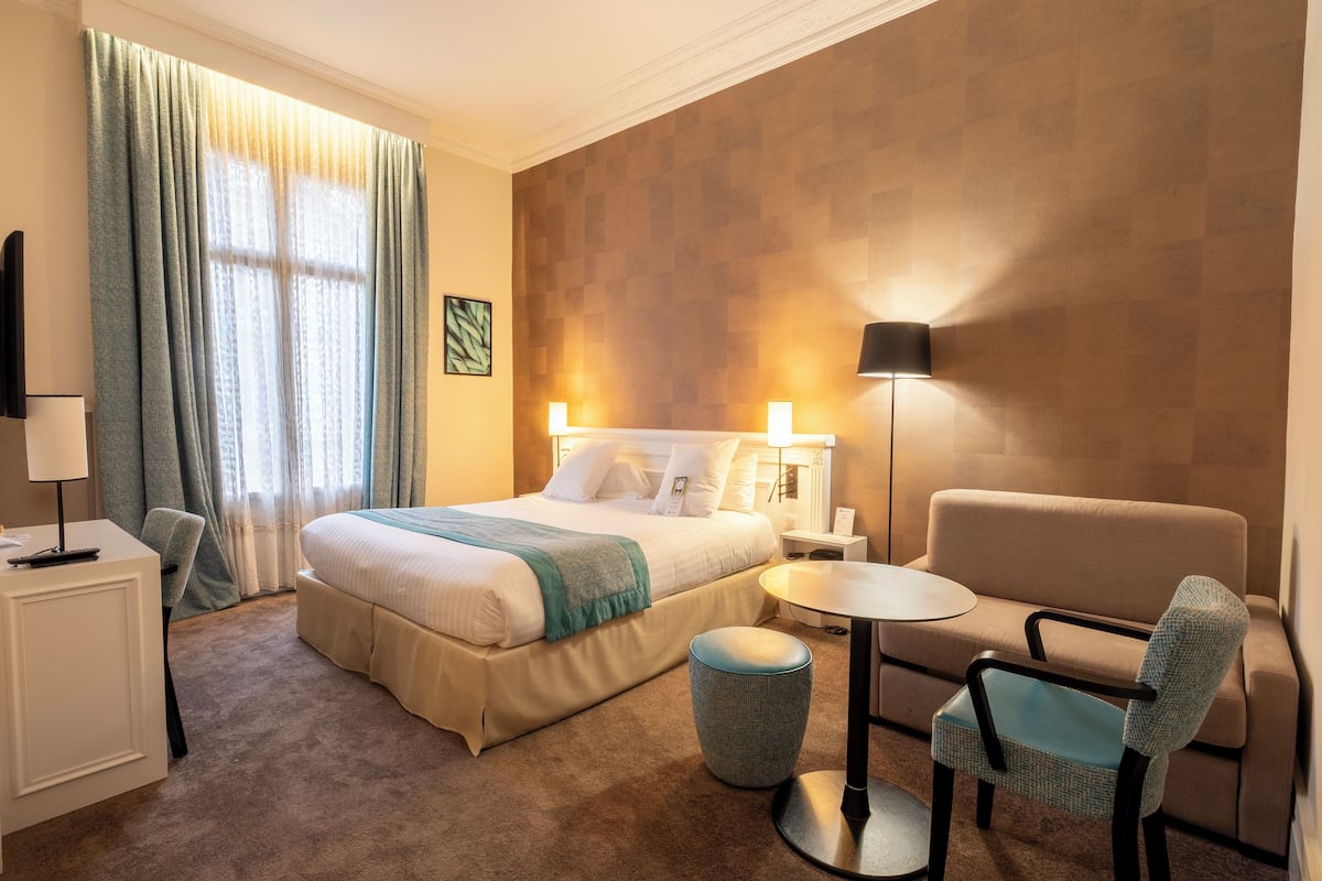 A hotel room with a bed, a sofa, a small table, a lamp, and a TV.