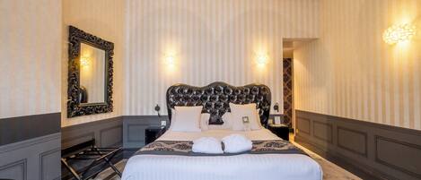 A hotel room with a large bed, a dresser, a mirror, and two wall sconces.