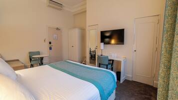 A hotel room with a large bed, a desk with a chair, a television, and a door.
