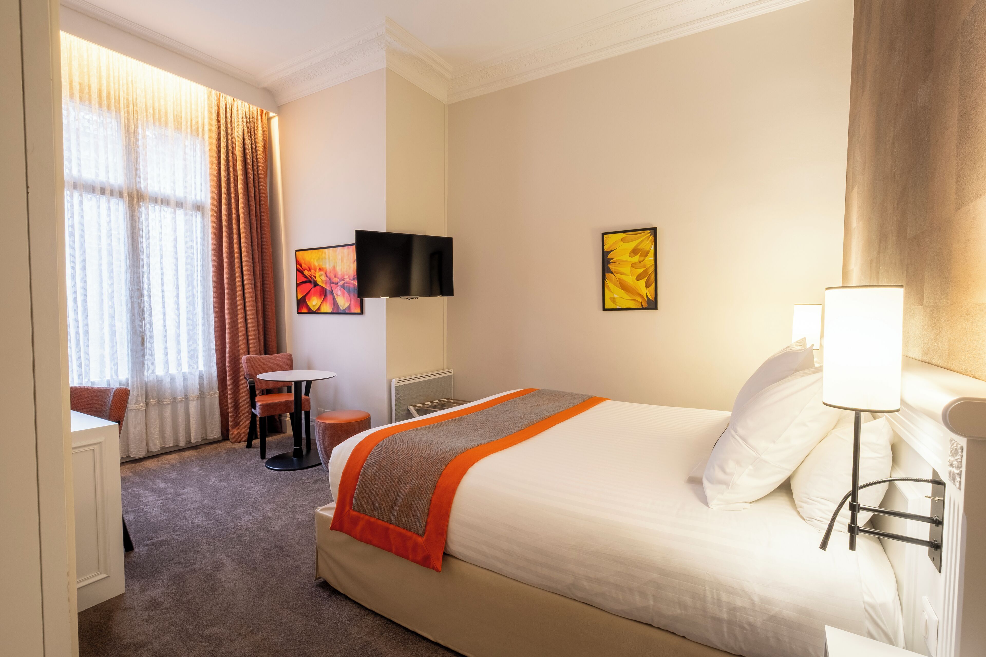A hotel room with a large bed, a desk, a chair, a TV, and artwork on the walls.