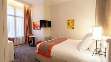 A hotel room with a large bed, a desk, a chair, a TV, and artwork on the walls.