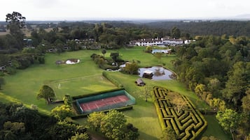 An aerial view of a golf course with a tennis court, a maze, and residential buildings in the background.