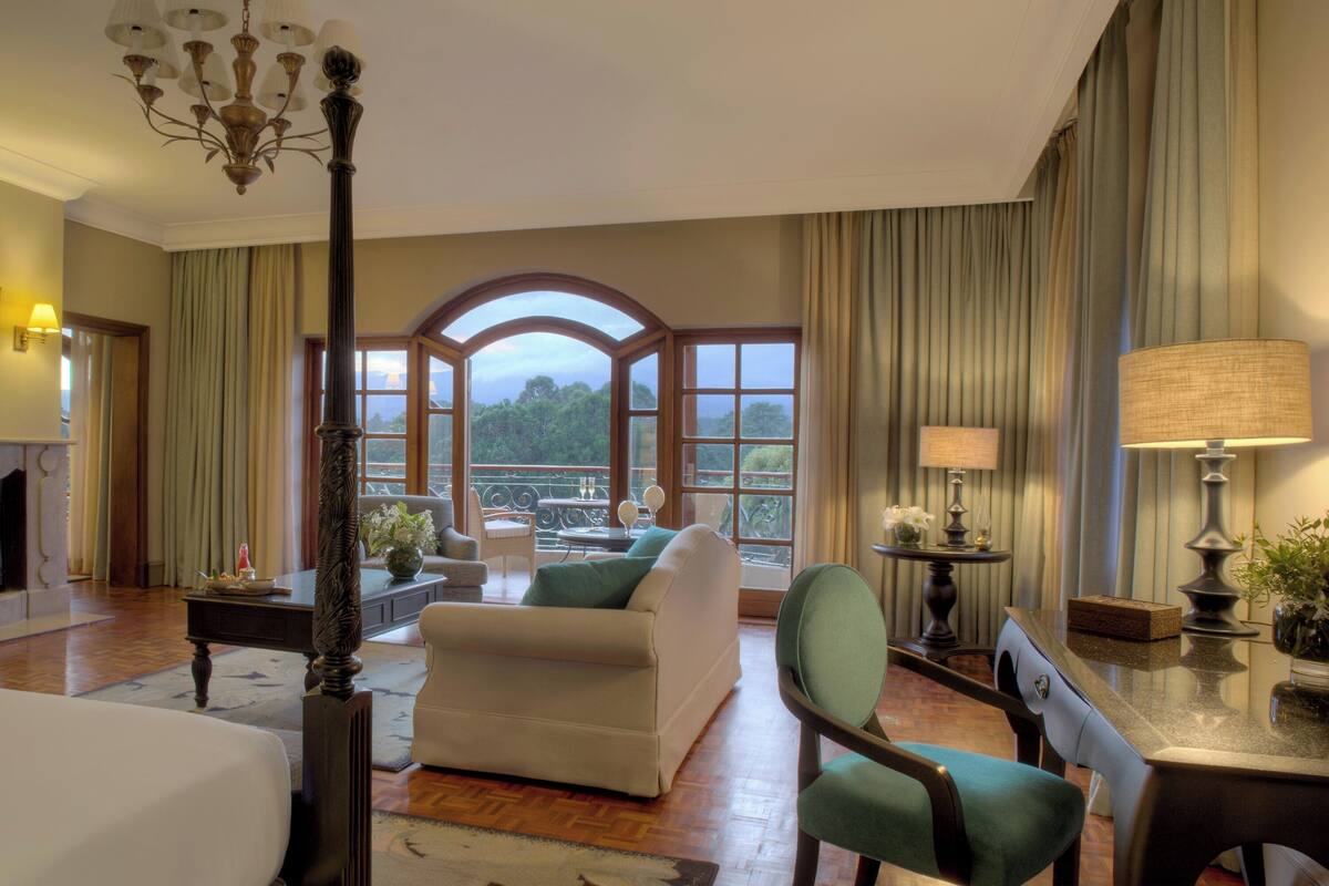 A spacious hotel room with a fireplace, a large window offering a scenic view, a comfortable sofa, and a dining area.