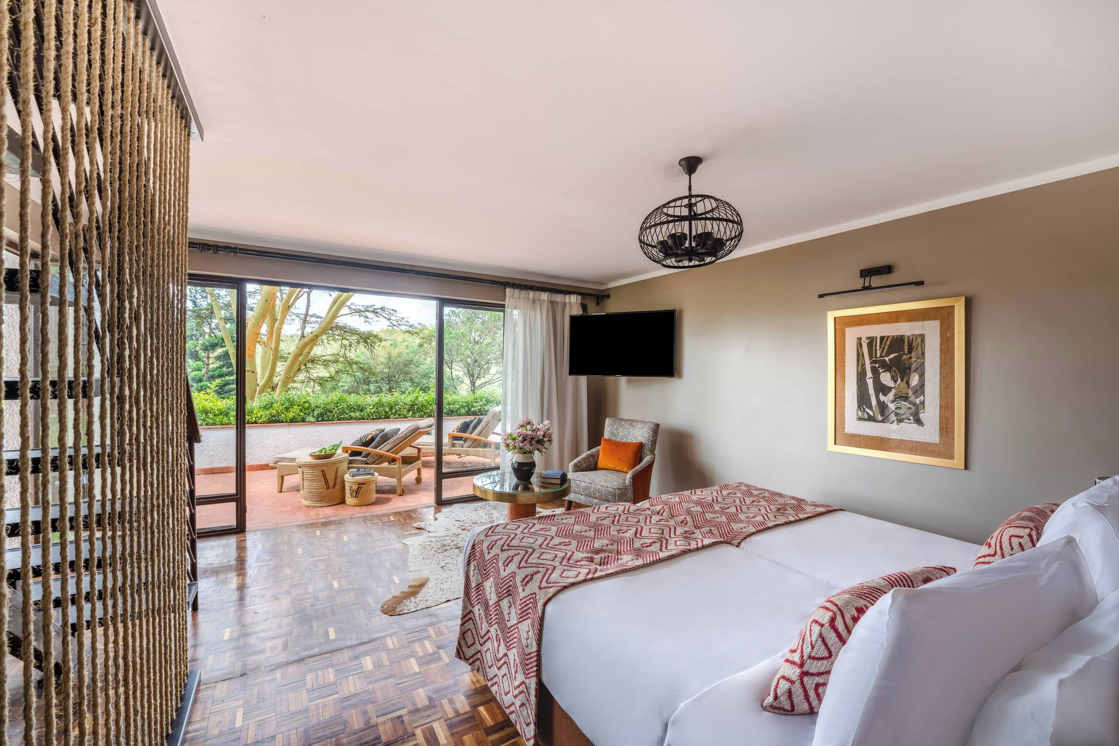 A spacious bedroom with a large bed, a television mounted on the wall, and a view of the outdoors through a sliding door.