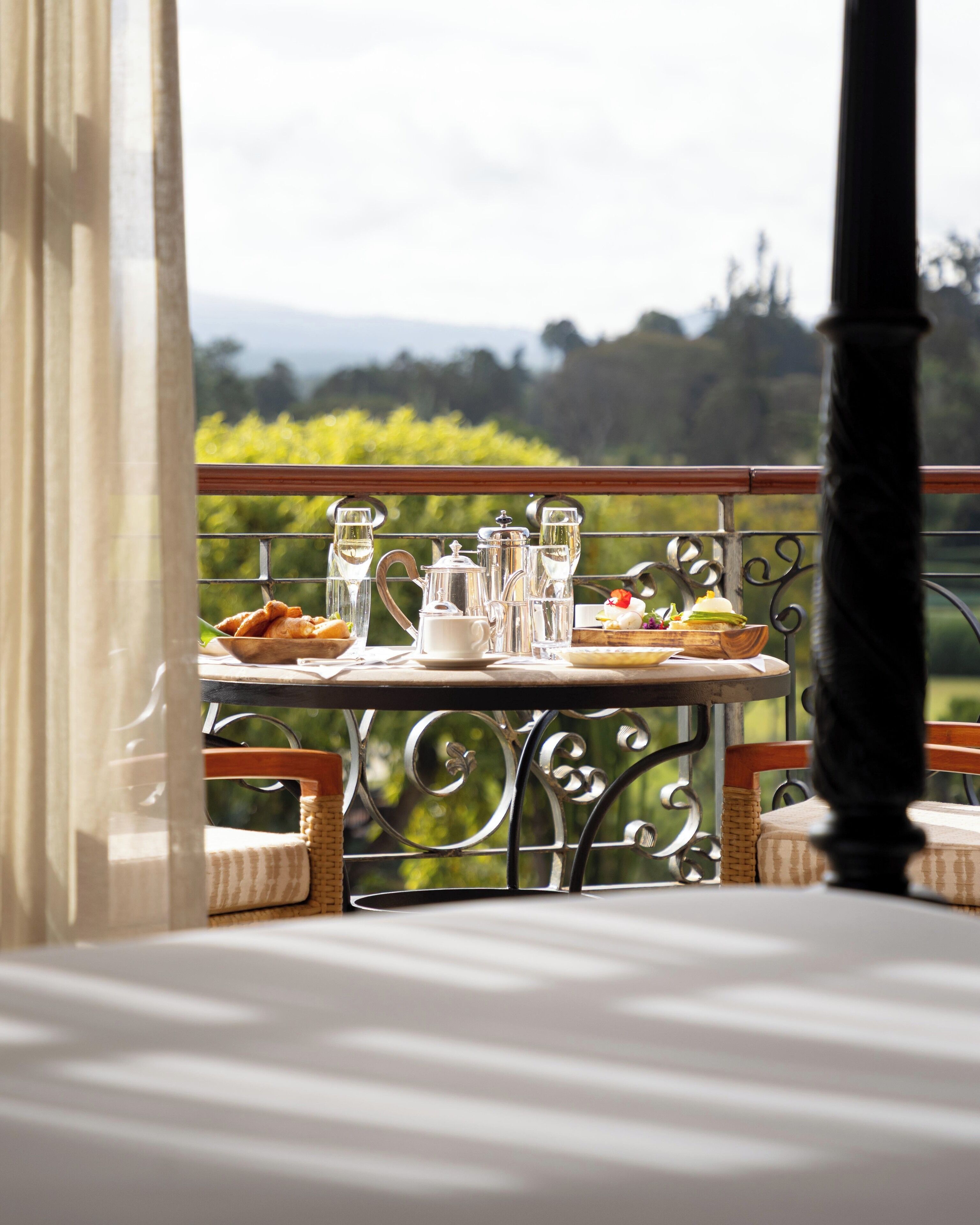 Une table placée sur un balcon, agrémentée d’une théière, de tasses et d’une assiette de nourriture, et offrant une vue sur un paysage magnifique.