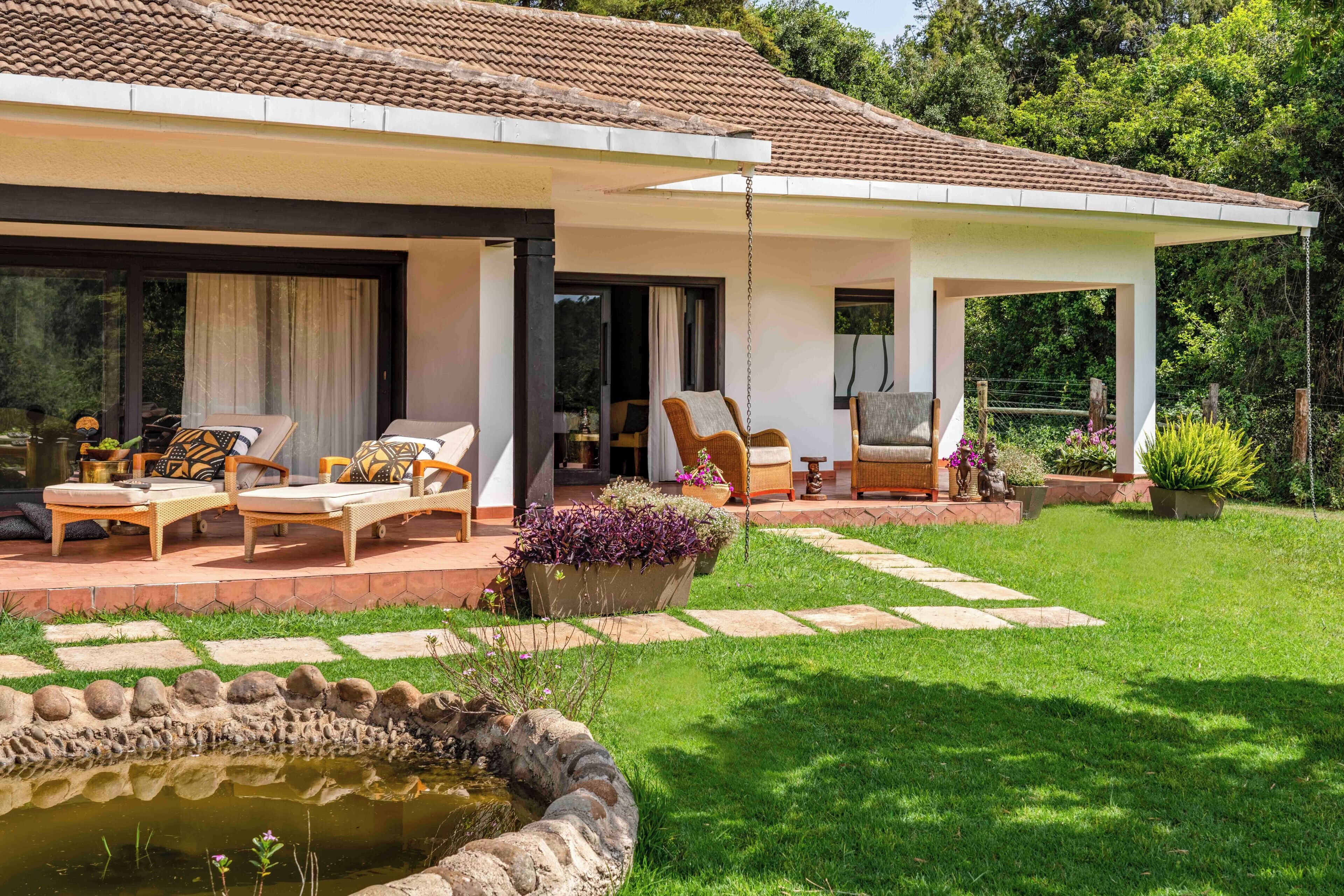 A modern house with a covered patio, outdoor seating area, and a small pond.