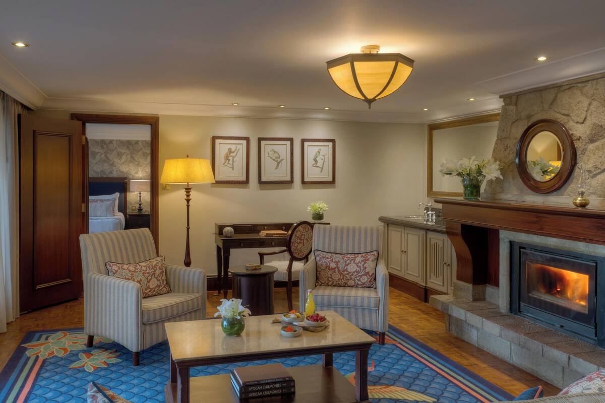 A hotel room with a fireplace, a dining area, and a living room with two armchairs and a coffee table.