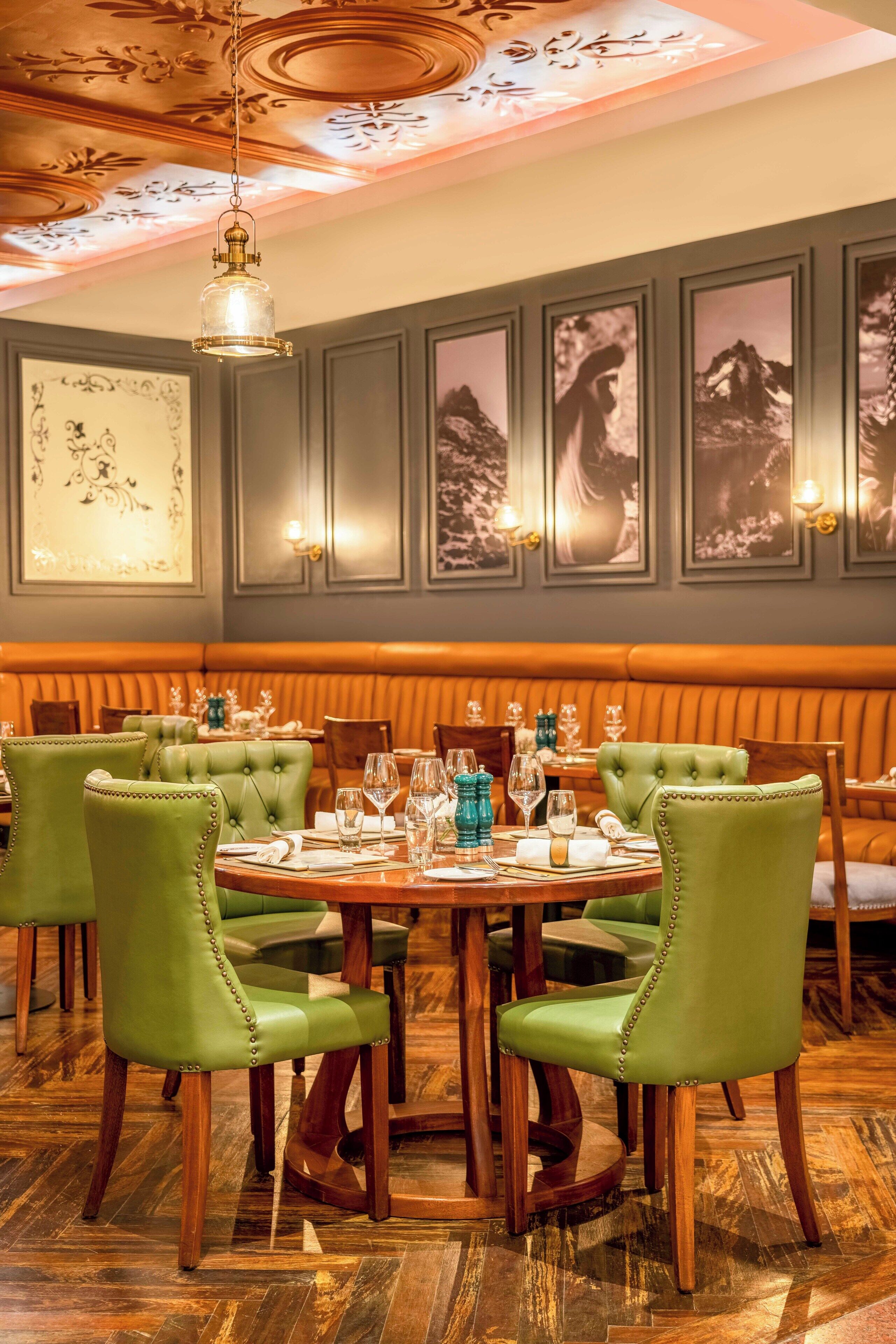 Un coin repas avec une table ronde dressée pour quatre personnes, entourée de chaises recouvertes d’un tissu vert.