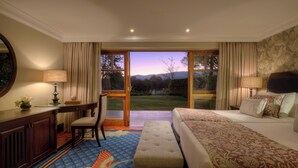A hotel room with a bed, a desk, a chair, and a view of the outdoors. - Fairmont Mount Kenya Safari (Nanyuki)
