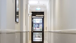A hallway with a checkered floor, white walls, and a door with glass panels. - Quest on Queen (Auckland)