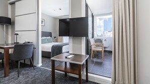 A hotel room with a bed, a desk with a chair, a TV, and a window with curtains. - Quest on Queen (Auckland)