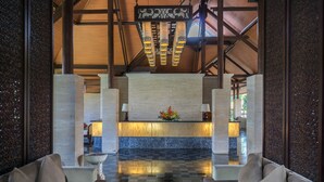 A lobby with a reception desk, two sofas, a decorative wall, and a chandelier. - Grand Balisani Suites Hotel (Keroboken Kelod)