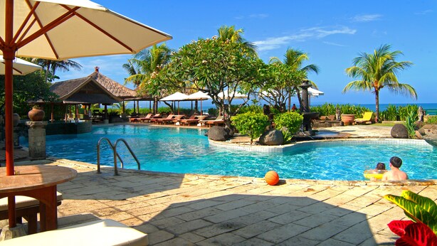 A pool area with lounge chairs, umbrellas, and a view of the ocean. - Grand Balisani Suites Hotel (Keroboken Kelod)
