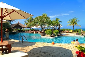 A pool area with lounge chairs, umbrellas, and a view of the ocean. - Grand Balisani Suites Hotel (Keroboken Kelod)
